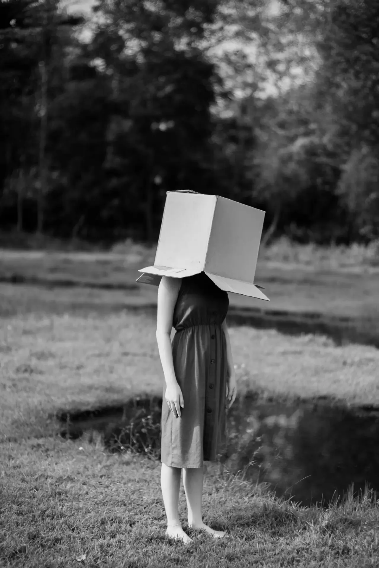 Image en noir et blanc d'une femme debout, un carton posé sur la tête