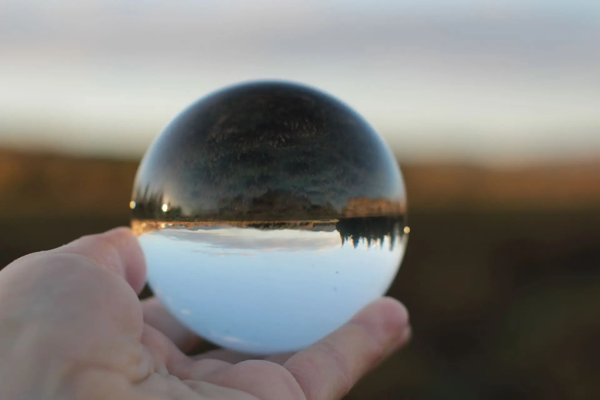 Boule de cristal posé dans une main qui reflette un paysage a travers
